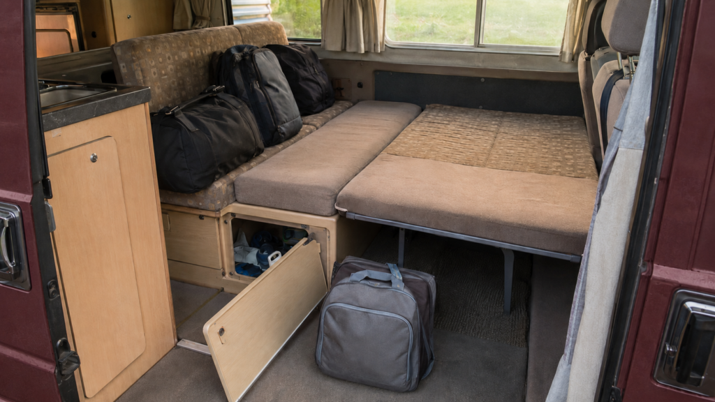 Interior de una furgoneta camper con bolsas y objetos que hay que mover para preparar la cama.