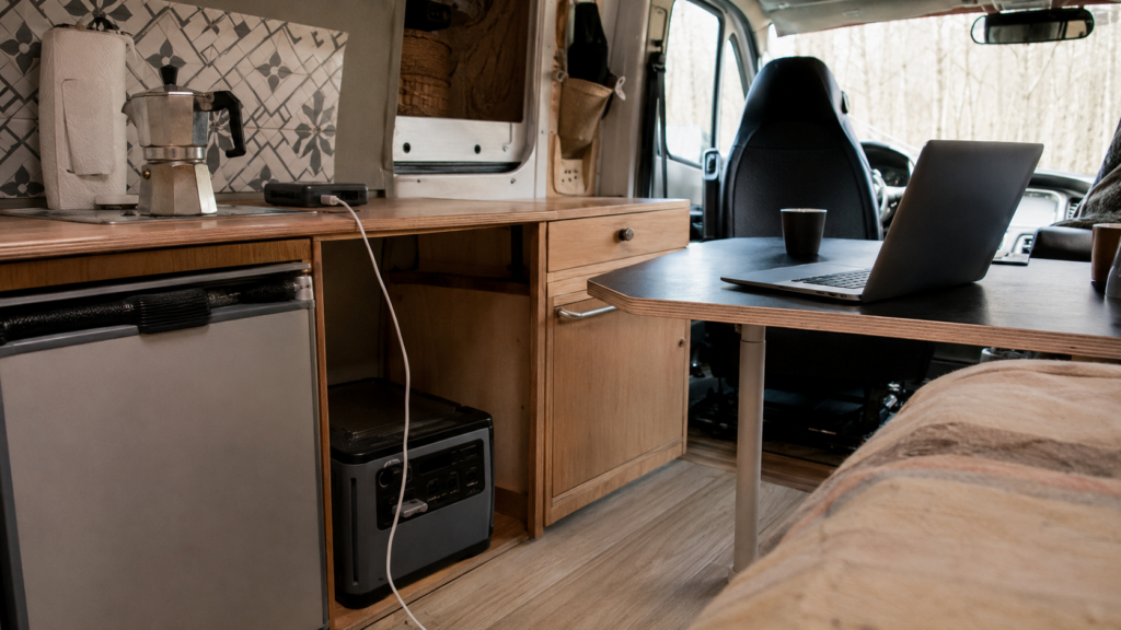 Interior de una furgoneta camper con una estación de energía portátil, un ordenador y un teléfono móvil cargando.