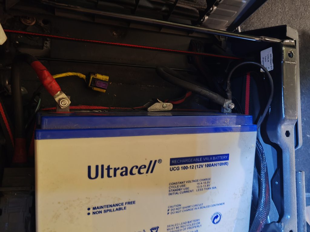 Batería AGM de 100 Ah instalada bajo uno de los asientos de la autocaravana, rodeada del cableado de la instalación eléctrica original.